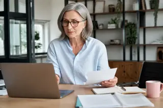 Confident woman in her mid-fifties working on a laptop in a bright, modern office, focused and professional atmosphere.